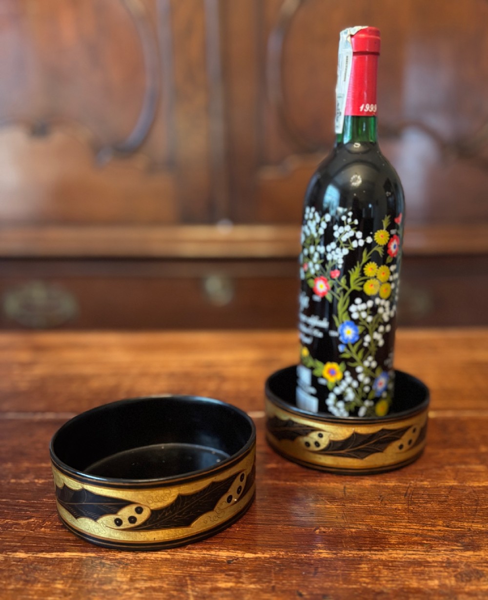 A pair of circular Regency black lacquered papier-mache wine coasters decorated with hand-painted gilded foliage motifs around the outer rim. View VIII