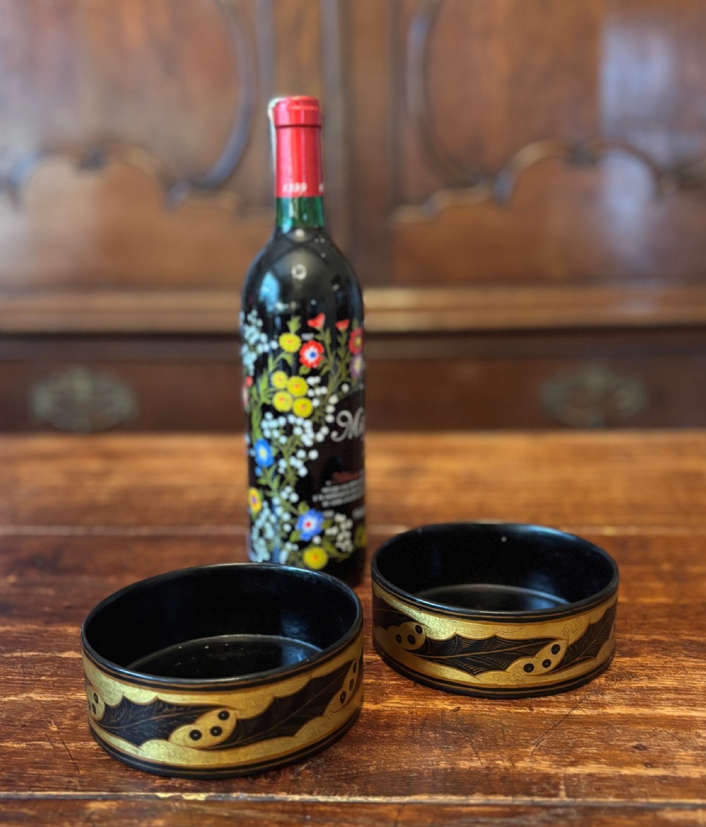A pair of circular Regency black lacquered papier-mache wine coasters decorated with hand-painted gilded foliage motifs around the outer rim. View XI