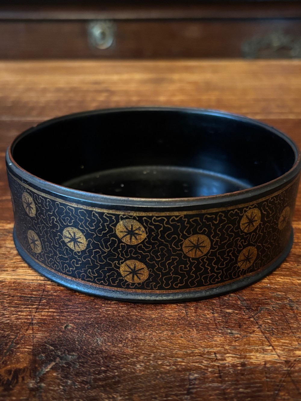 A circular black lacquered antique wine coaster decorated with gold star motifs and vermicelli patterns around the exterior side.