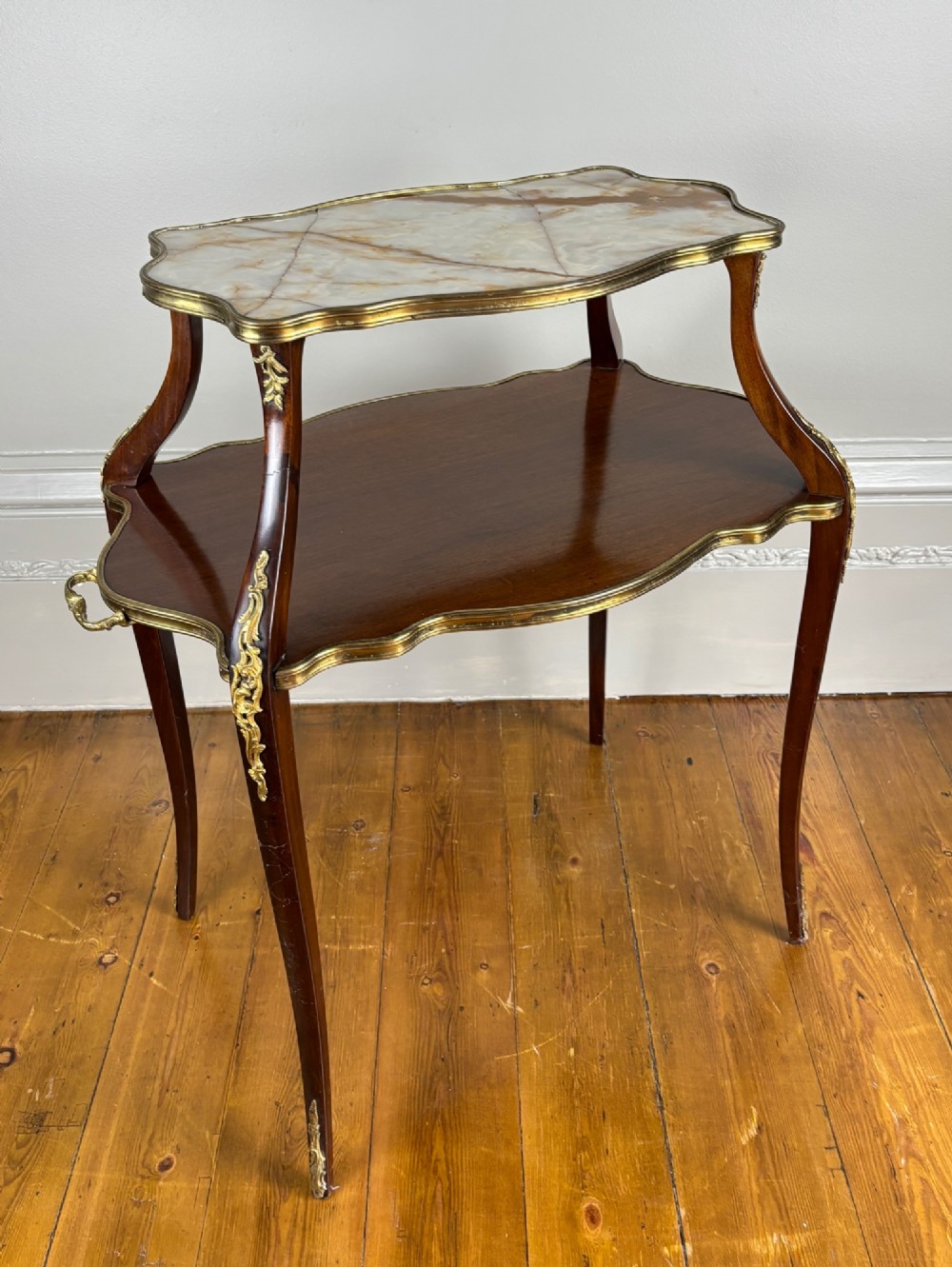 A French Napoleon III style two-tier tea table featuring an onyx inset top shelf, a mahogany lower shelf with side handles, cabriole legs, and gilded bronze mounts.