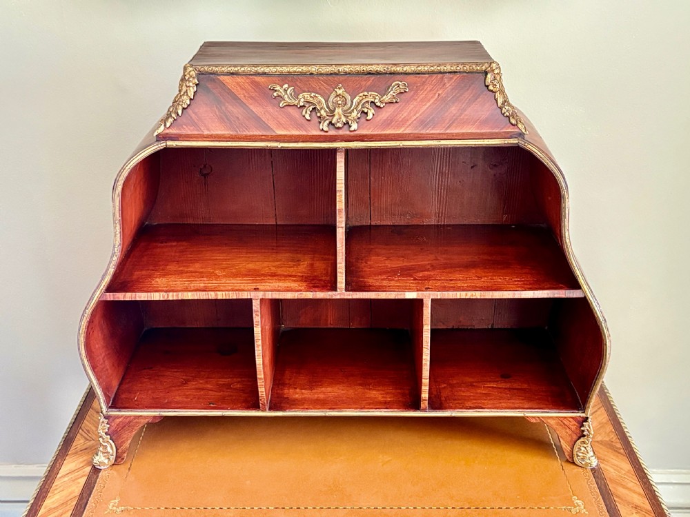 A Louis XV style rosewood desktop cartonnier with curved sides, gold-toned ormolu mounts, and open storage compartments.