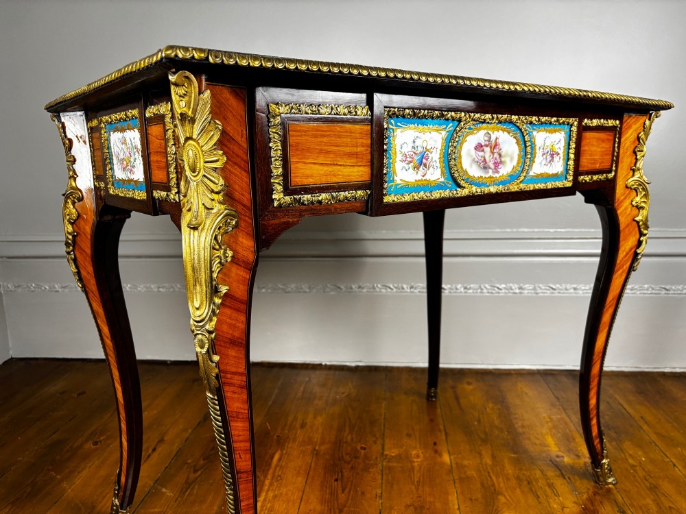 A Louis XV style rosewood writing table featuring cabriole legs, gilt bronze ormolu mounts, and turquoise porcelain plaques.