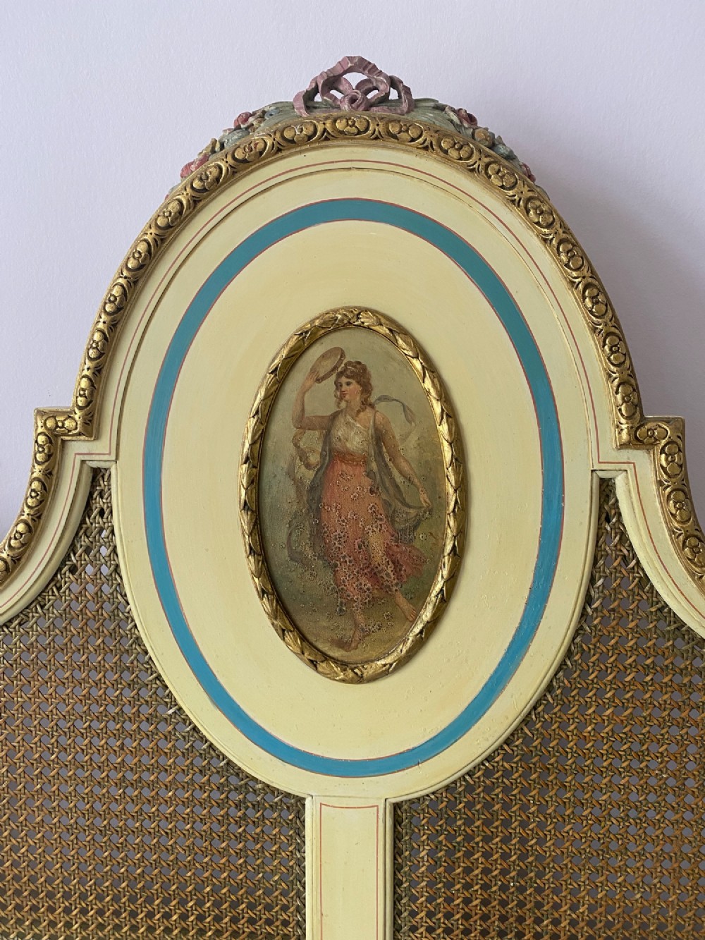 A pair of antique cream and gilt painted single beds featuring caned headboards with central painted portrait medallions and carved paw feet. View III
