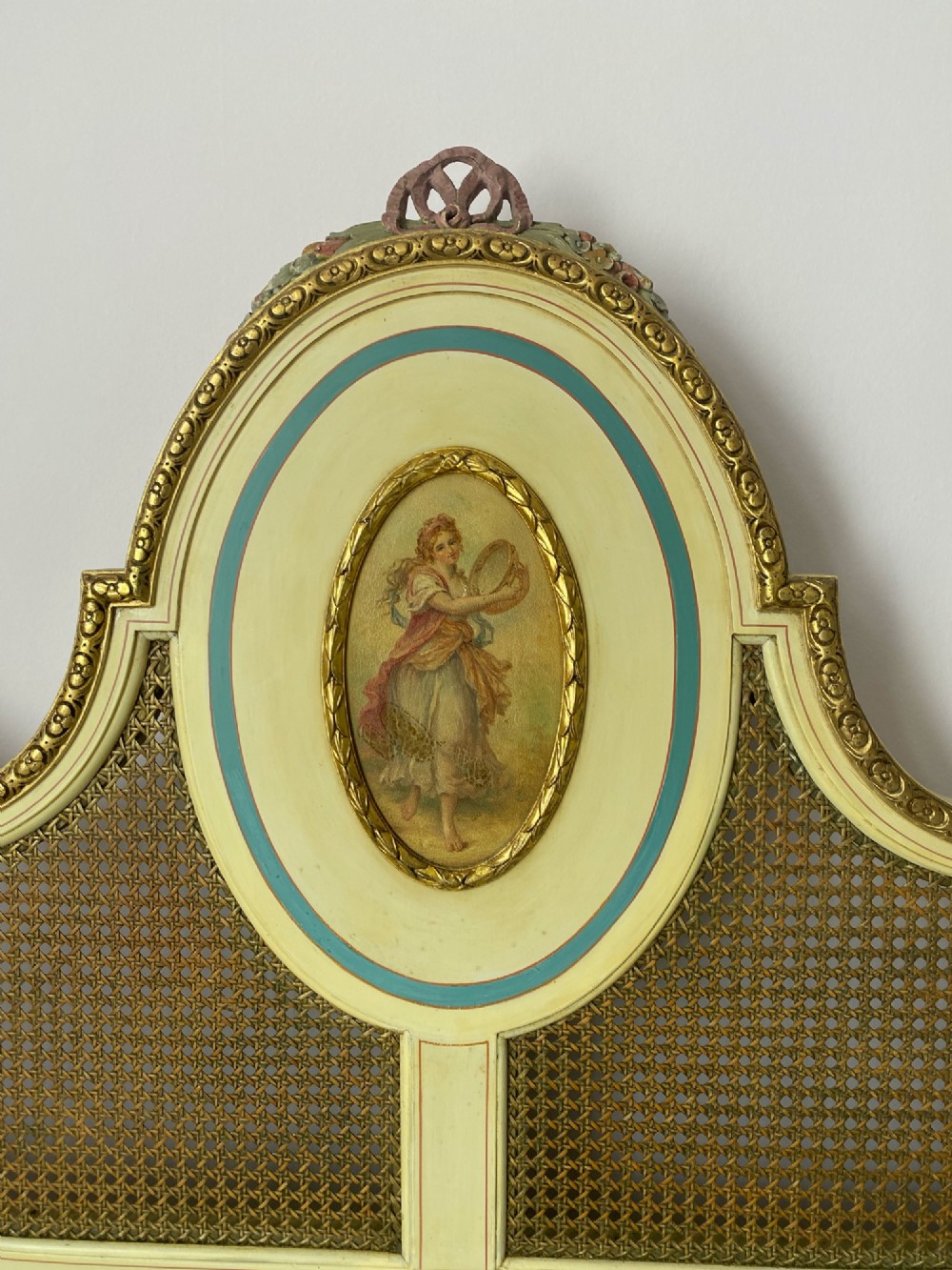 A pair of antique cream and gilt painted single beds featuring caned headboards with central painted portrait medallions and carved paw feet. View V