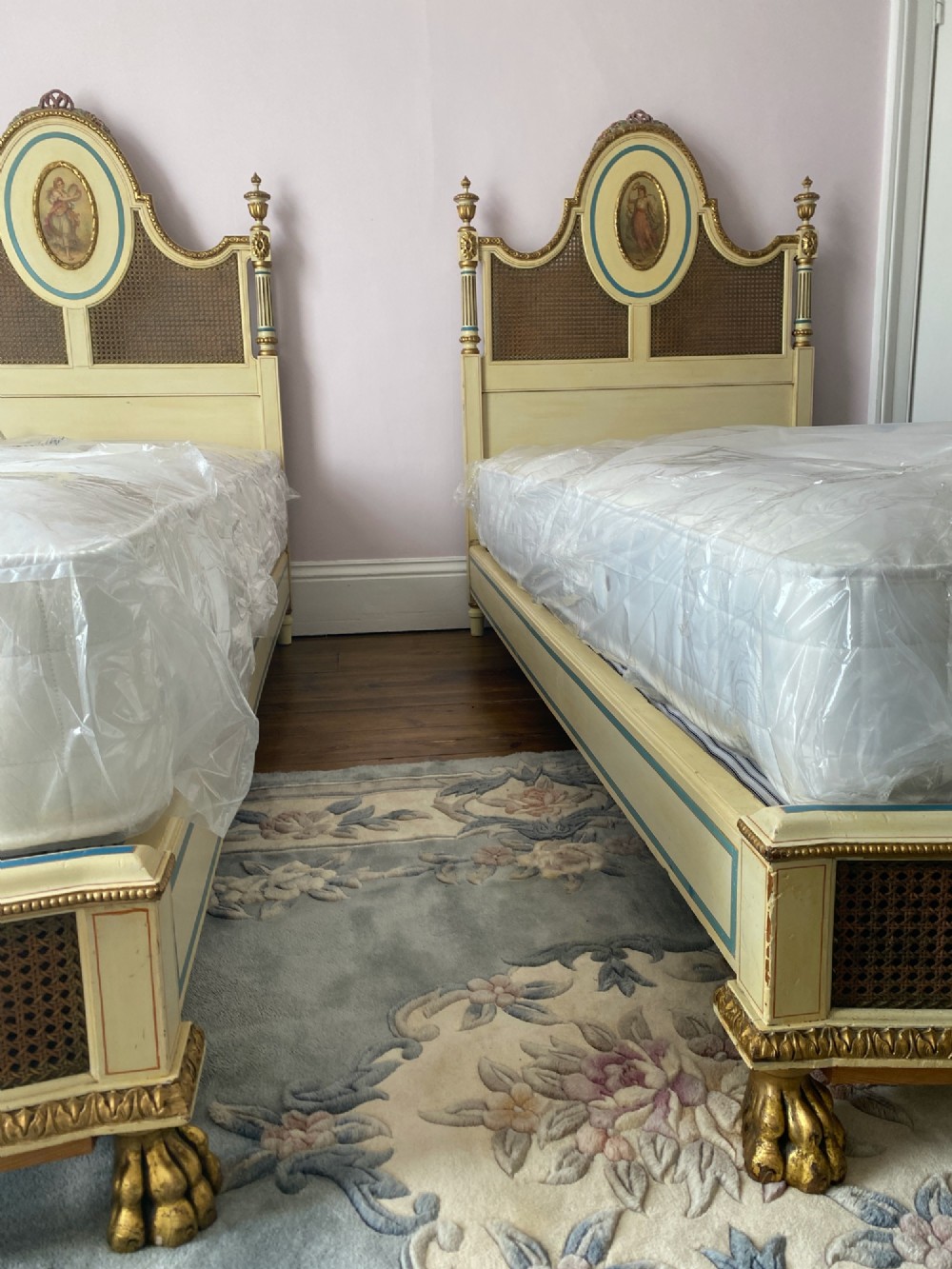 A pair of antique cream and gilt painted single beds featuring caned headboards with central painted portrait medallions and carved paw feet. View VII