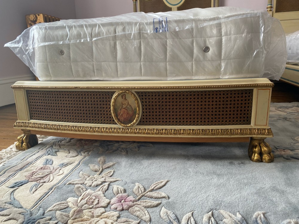 A pair of antique cream and gilt painted single beds featuring caned headboards with central painted portrait medallions and carved paw feet. View VIII