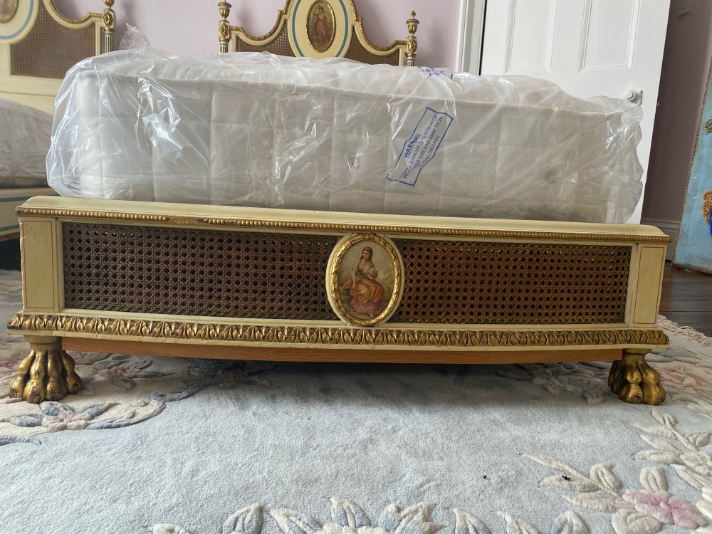 A pair of antique cream and gilt painted single beds featuring caned headboards with central painted portrait medallions and carved paw feet. View XI