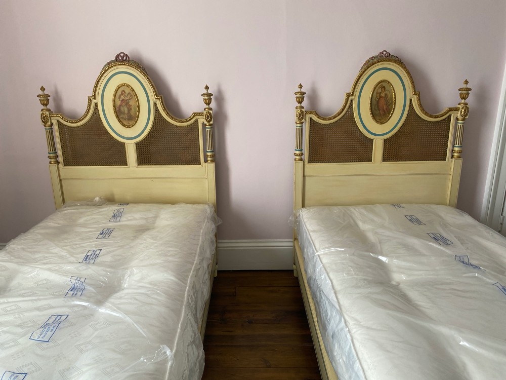 A pair of antique cream and gilt painted single beds featuring caned headboards with central painted portrait medallions and carved paw feet. View XIII