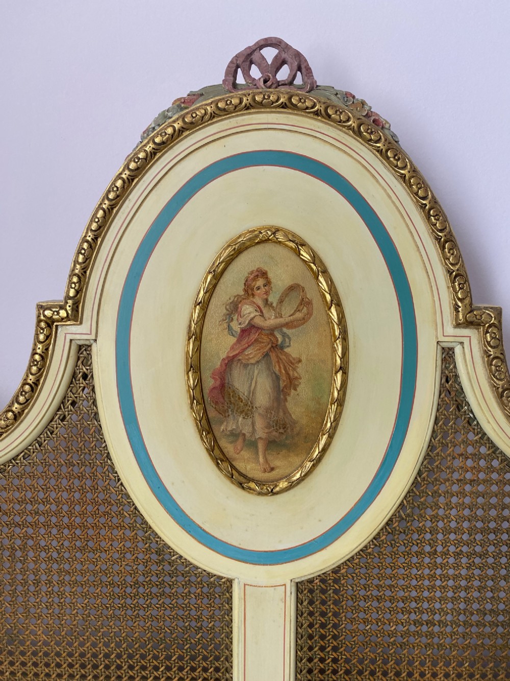 A pair of antique cream and gilt painted single beds featuring caned headboards with central painted portrait medallions and carved paw feet. View XV
