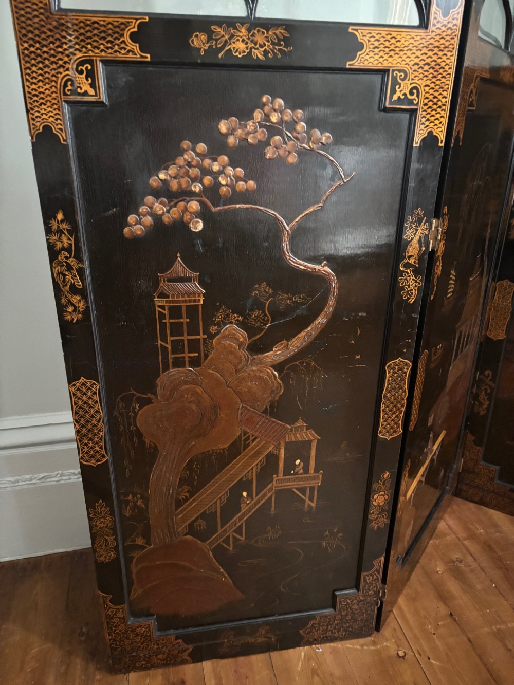 A four-fold black lacquered screen with Chinese Chippendale fretwork crestings, glazed upper panels, and incised gold chinoiserie landscape scenes. View VI