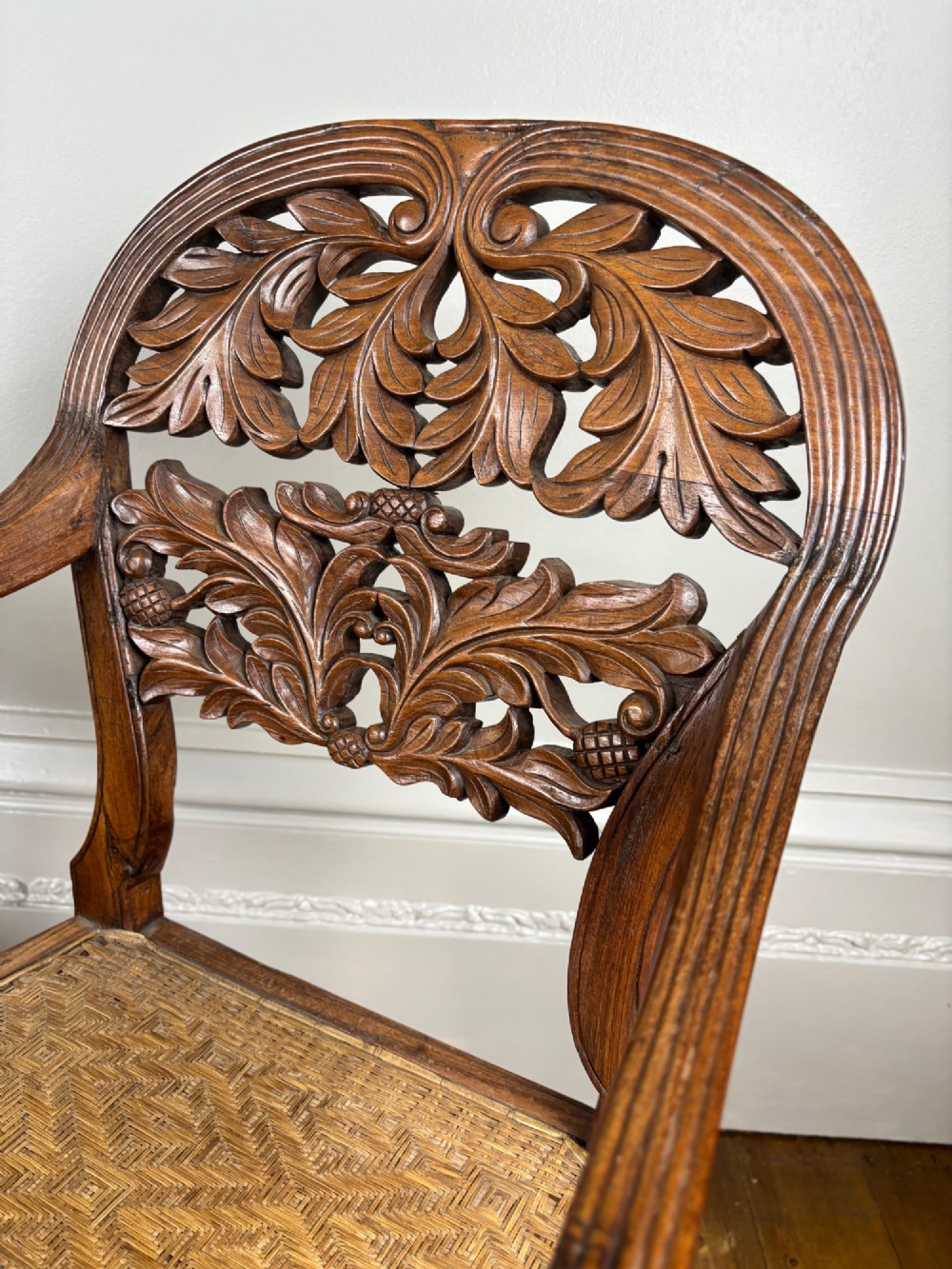 A pair of carved hardwood open armchairs featuring intricate openwork foliate backrests, swept arms, woven cane seats, and turned front legs. View III