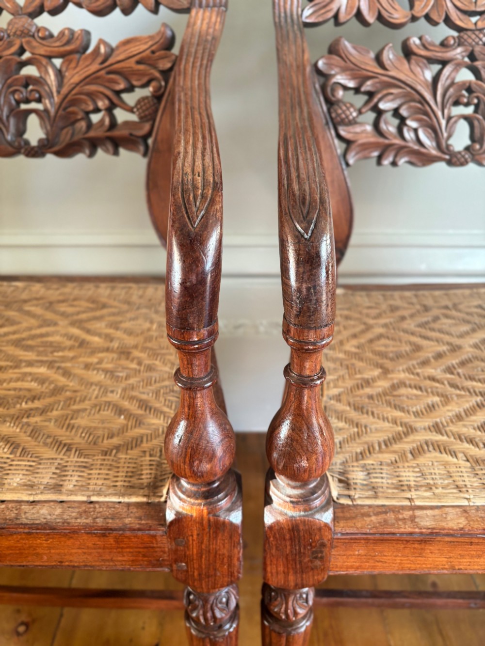 A pair of carved hardwood open armchairs featuring intricate openwork foliate backrests, swept arms, woven cane seats, and turned front legs. View VI