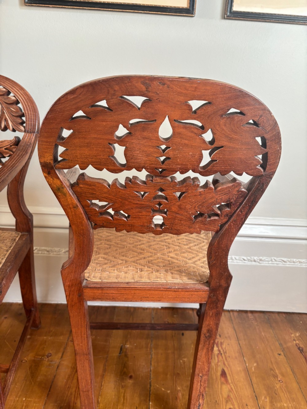 A pair of carved hardwood open armchairs featuring intricate openwork foliate backrests, swept arms, woven cane seats, and turned front legs. View VII