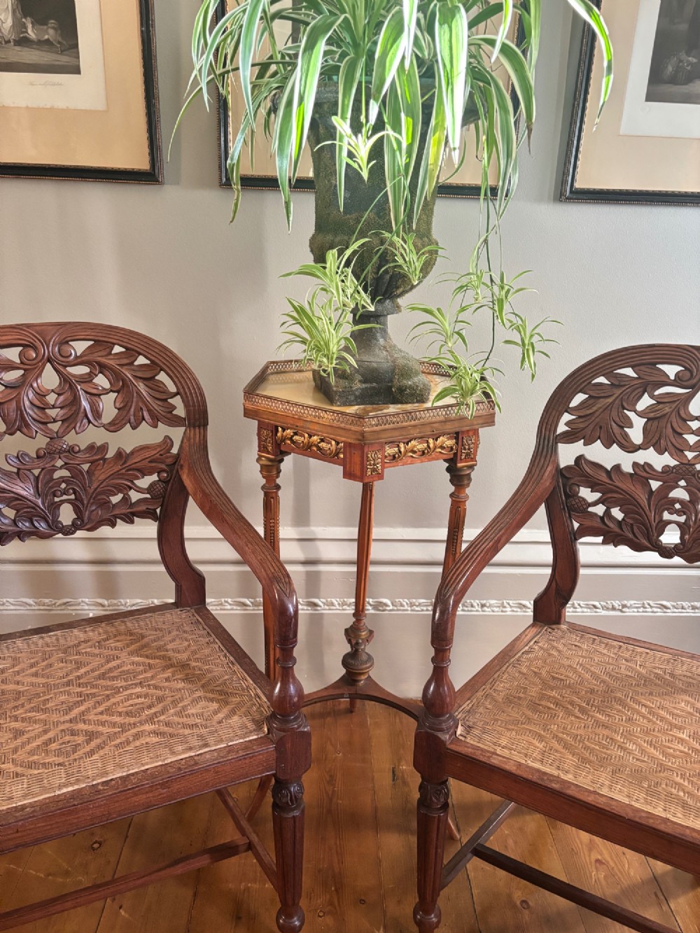 A pair of carved hardwood open armchairs featuring intricate openwork foliate backrests, swept arms, woven cane seats, and turned front legs. View X