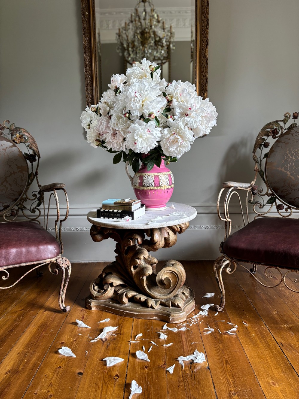 A pair of French wrought iron armchairs featuring cream painted scrolled frames, polychrome floral accents around oval backrests, and burgundy leather seats. View V