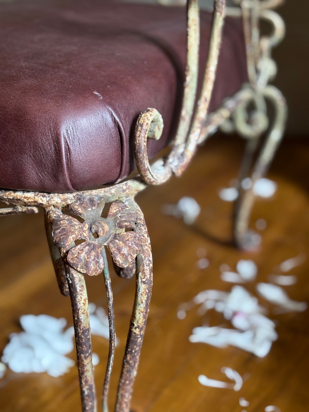 A pair of French wrought iron armchairs featuring cream painted scrolled frames, polychrome floral accents around oval backrests, and burgundy leather seats. View VII
