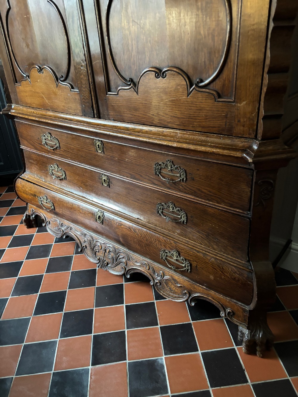 An 18th-century Dutch carved oak linen press featuring contoured panel doors, a carved cresting pediment, brass handles, and a bombee lower section with drawers. View II