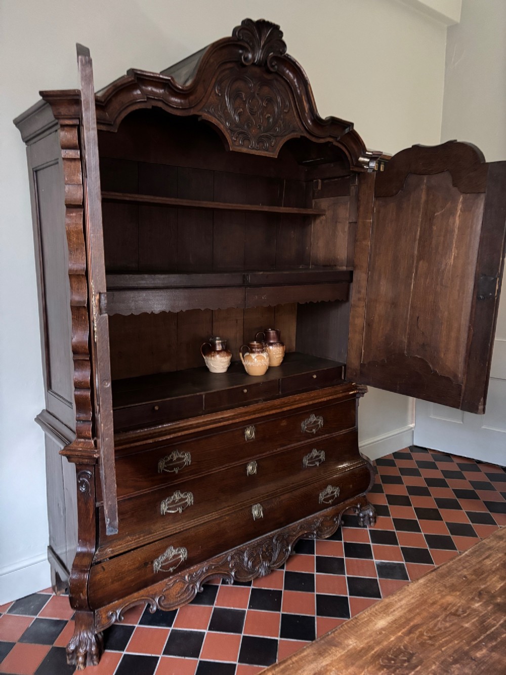 An 18th-century Dutch carved oak linen press featuring contoured panel doors, a carved cresting pediment, brass handles, and a bombee lower section with drawers. View VII