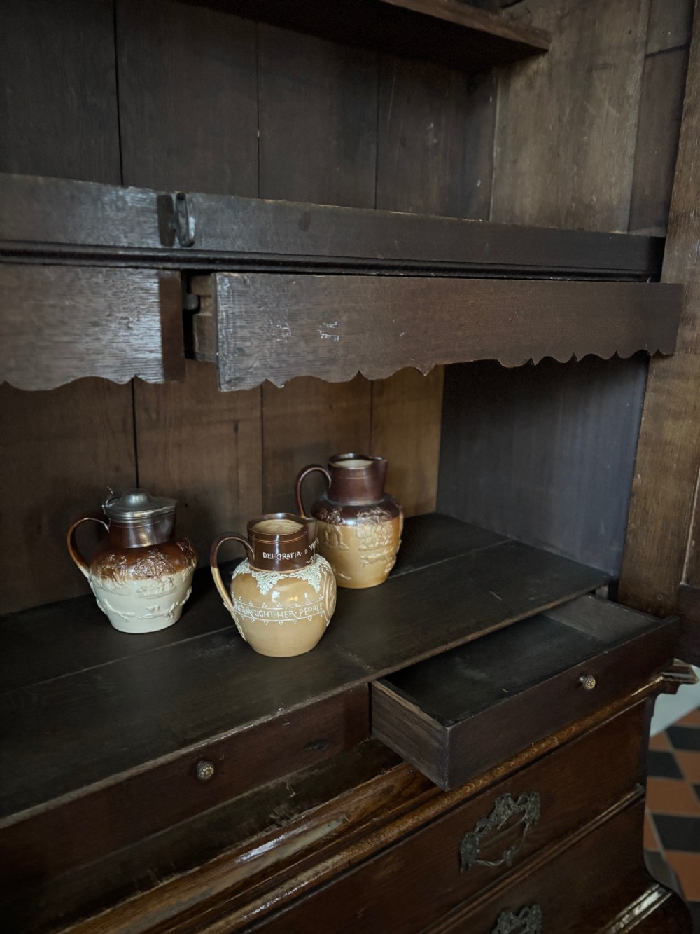 An 18th-century Dutch carved oak linen press featuring contoured panel doors, a carved cresting pediment, brass handles, and a bombee lower section with drawers. View IX