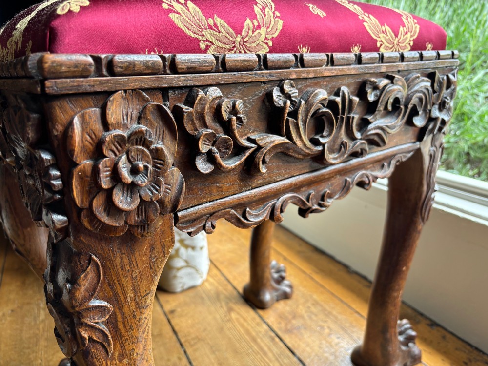 A Victorian Chippendale style carved wooden stool featuring cabriole legs with ball-and-claw feet and a rich burgundy upholstered seat patterned with gold wreaths. View II