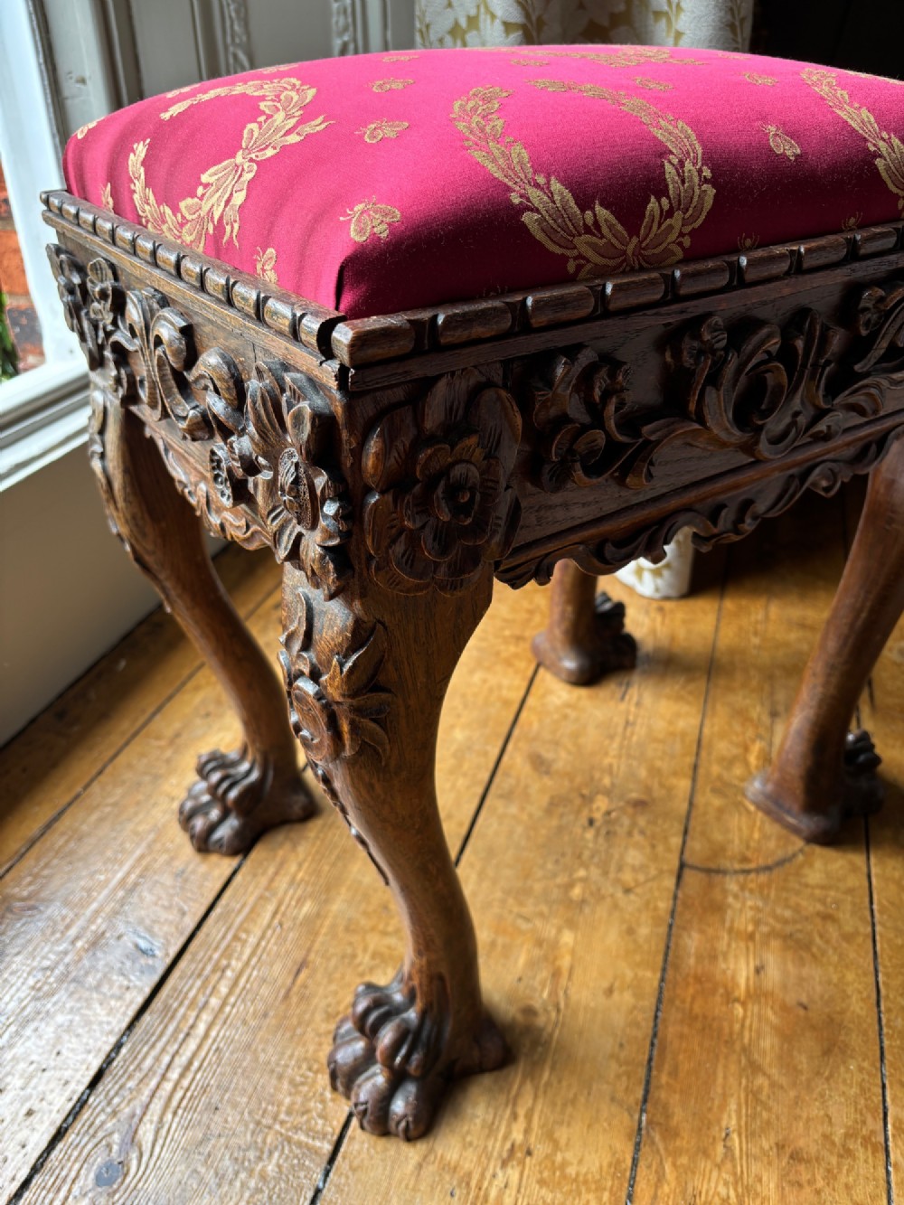 A Victorian Chippendale style carved wooden stool featuring cabriole legs with ball-and-claw feet and a rich burgundy upholstered seat patterned with gold wreaths. View IV