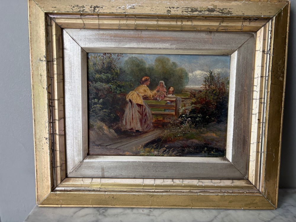 A small 19th-century style oil painting on board depicting a woman and children near a rustic wooden fence, set in a wide gilded frame. View II