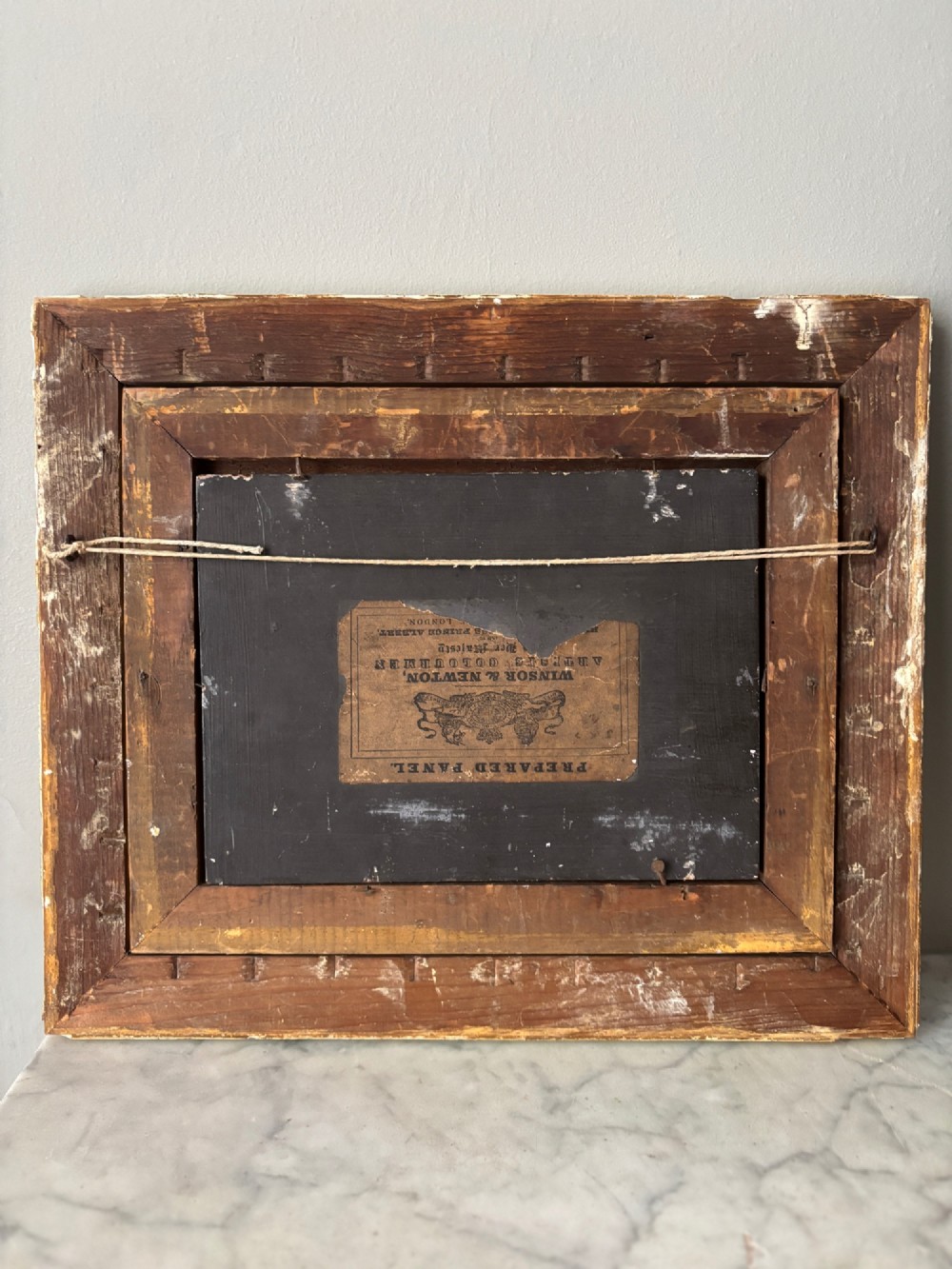 A small 19th-century style oil painting on board depicting a woman and children near a rustic wooden fence, set in a wide gilded frame. View IV