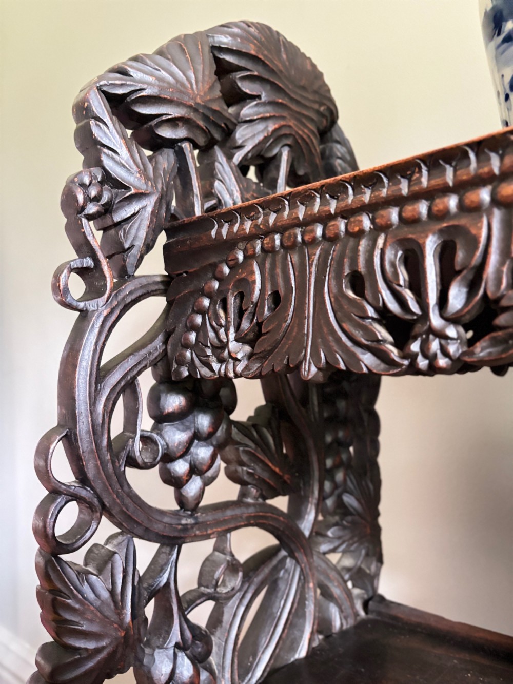 A tall mid-19th-century Anglo-Indian padauk wood shelving unit with three open tiers featuring deeply carved foliate aprons and intricate side supports. View VI