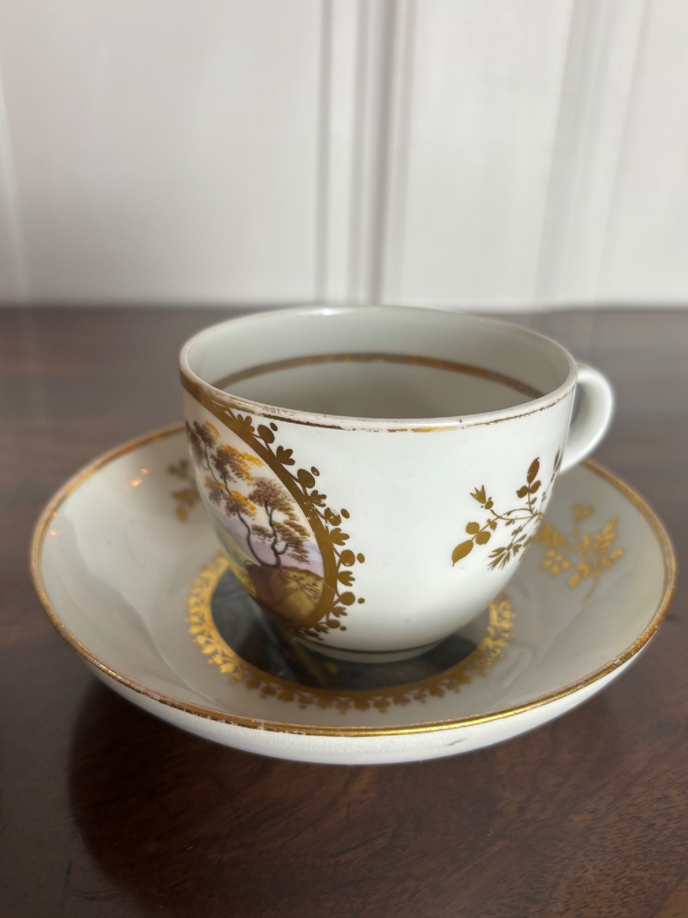 A pair of white Georgian porcelain teacups and saucers with hand-painted landscape scenes enclosed within gilded foliate borders. View VII