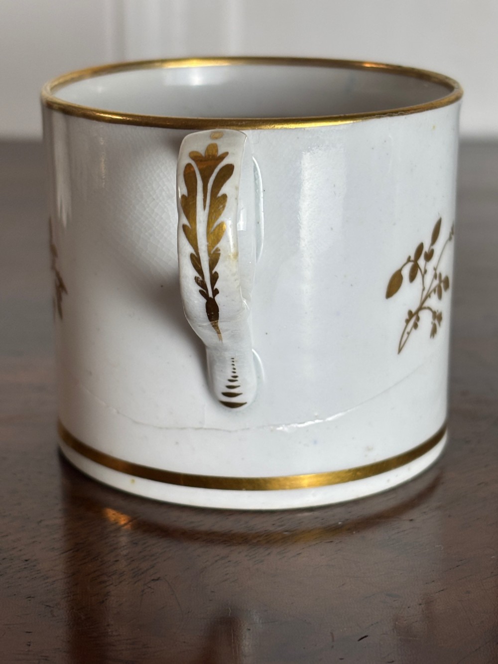 A pair of early nineteenth-century white porcelain coffee cans featuring hand-painted oval landscape vignettes framed with gilded borders. View IV