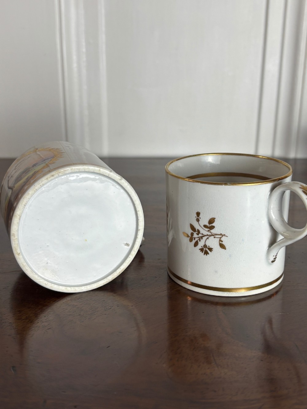 A pair of early nineteenth-century white porcelain coffee cans featuring hand-painted oval landscape vignettes framed with gilded borders. View VI