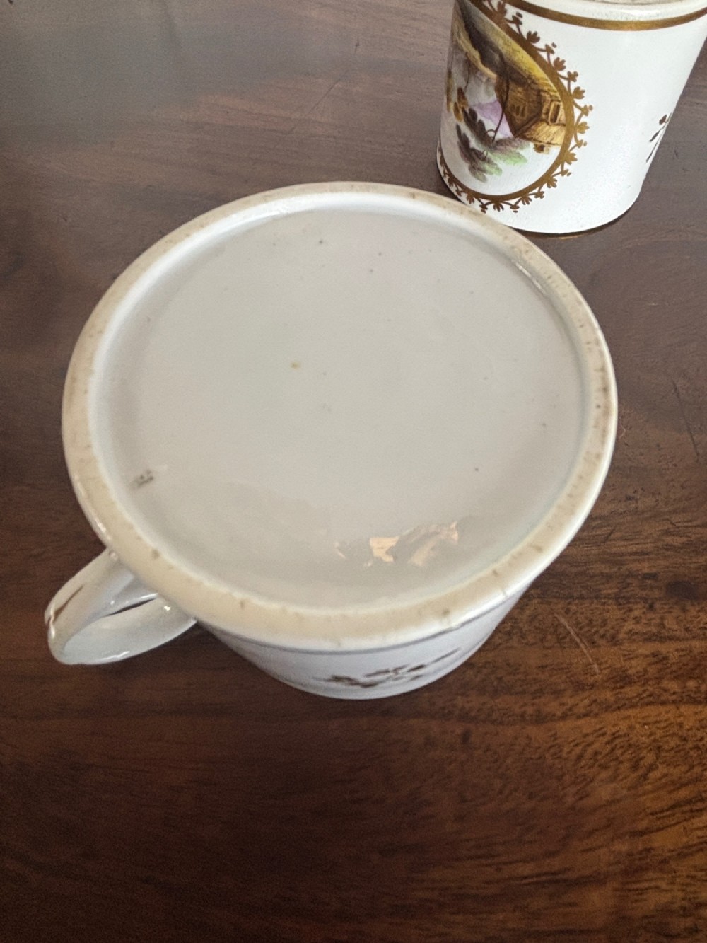 A pair of early nineteenth-century white porcelain coffee cans featuring hand-painted oval landscape vignettes framed with gilded borders. View IX