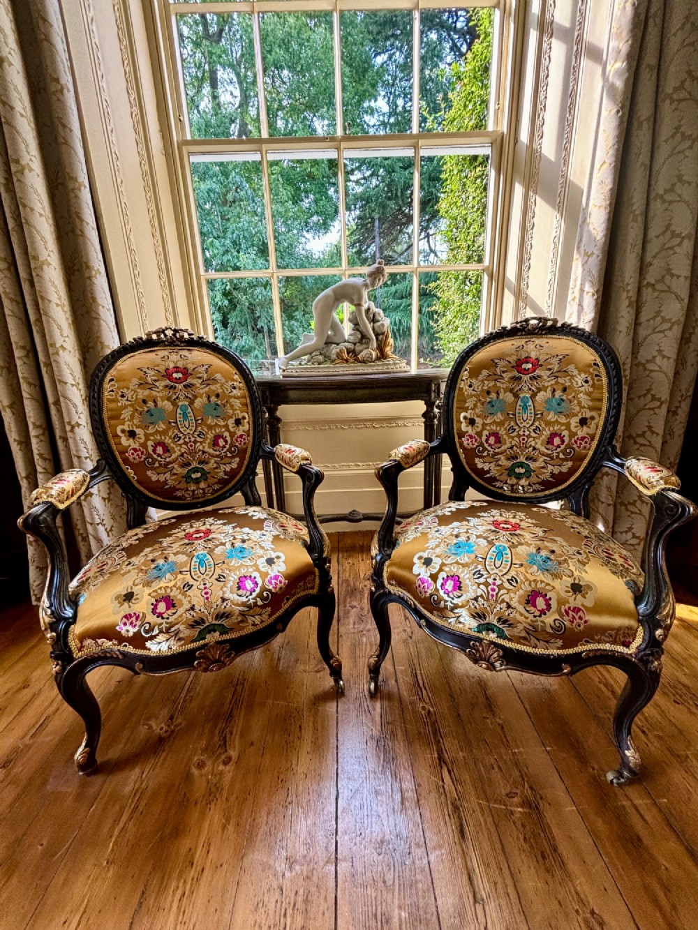 A pair of 19th-century French open armchairs with dark carved walnut frames, cabriole legs, and ornate gold silk brocade upholstery featuring floral motifs.