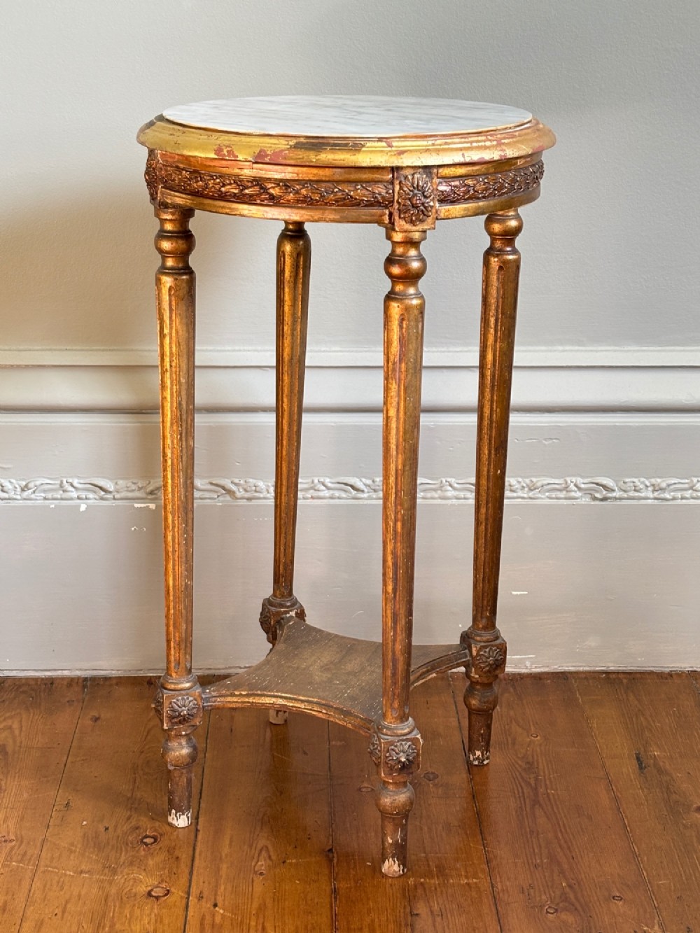 A French circa 1820 circular giltwood side table featuring a white marble top, fluted tapered legs, rosette carvings, and a low curved stretcher. View II