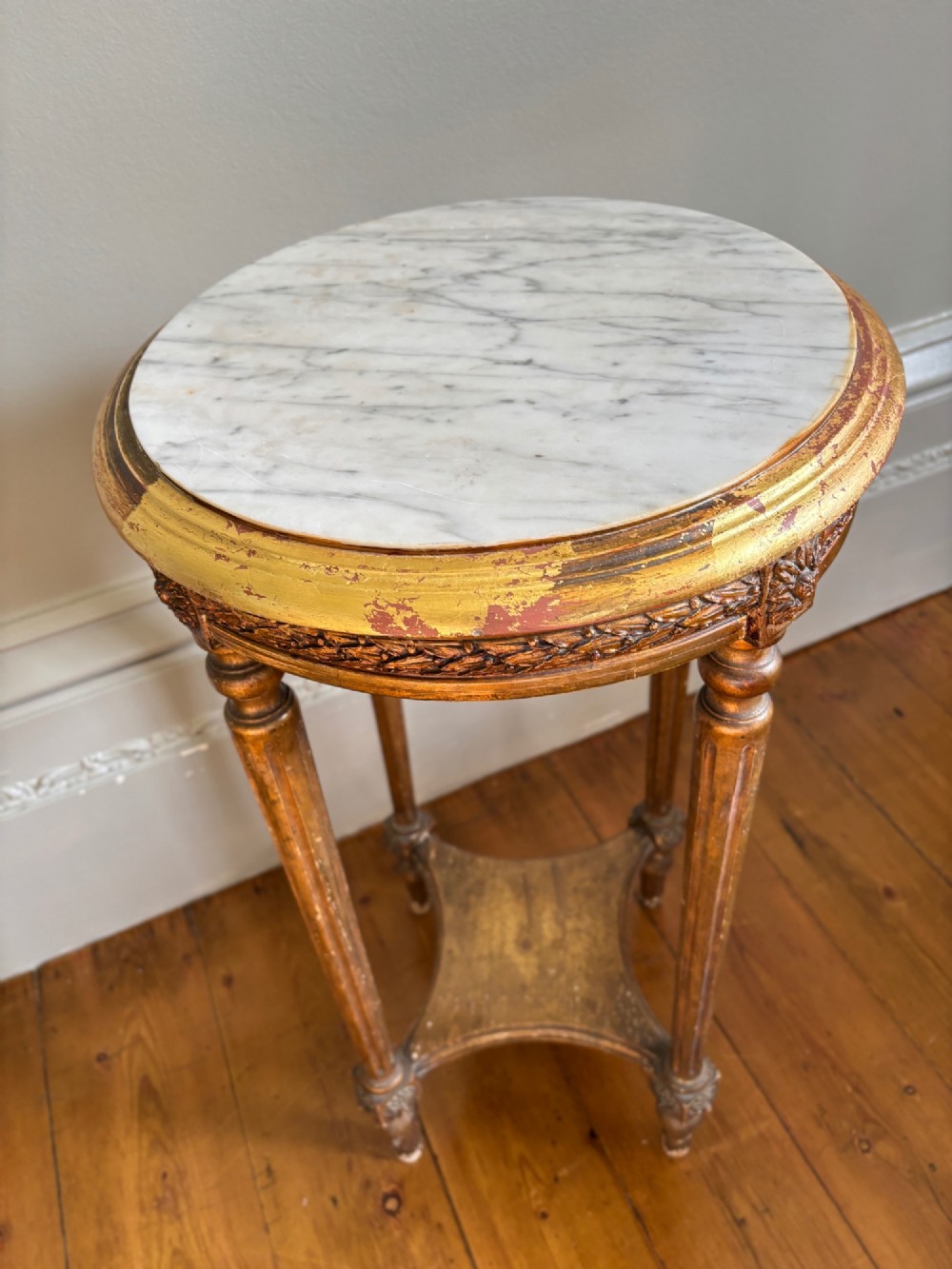 A French circa 1820 circular giltwood side table featuring a white marble top, fluted tapered legs, rosette carvings, and a low curved stretcher. View V