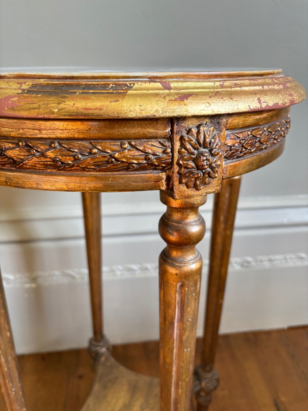 A French circa 1820 circular giltwood side table featuring a white marble top, fluted tapered legs, rosette carvings, and a low curved stretcher. View VI