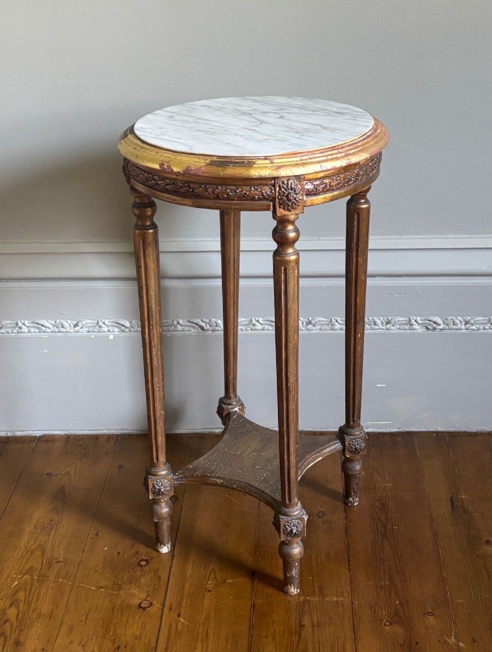 A French circa 1820 circular giltwood side table featuring a white marble top, fluted tapered legs, rosette carvings, and a low curved stretcher.