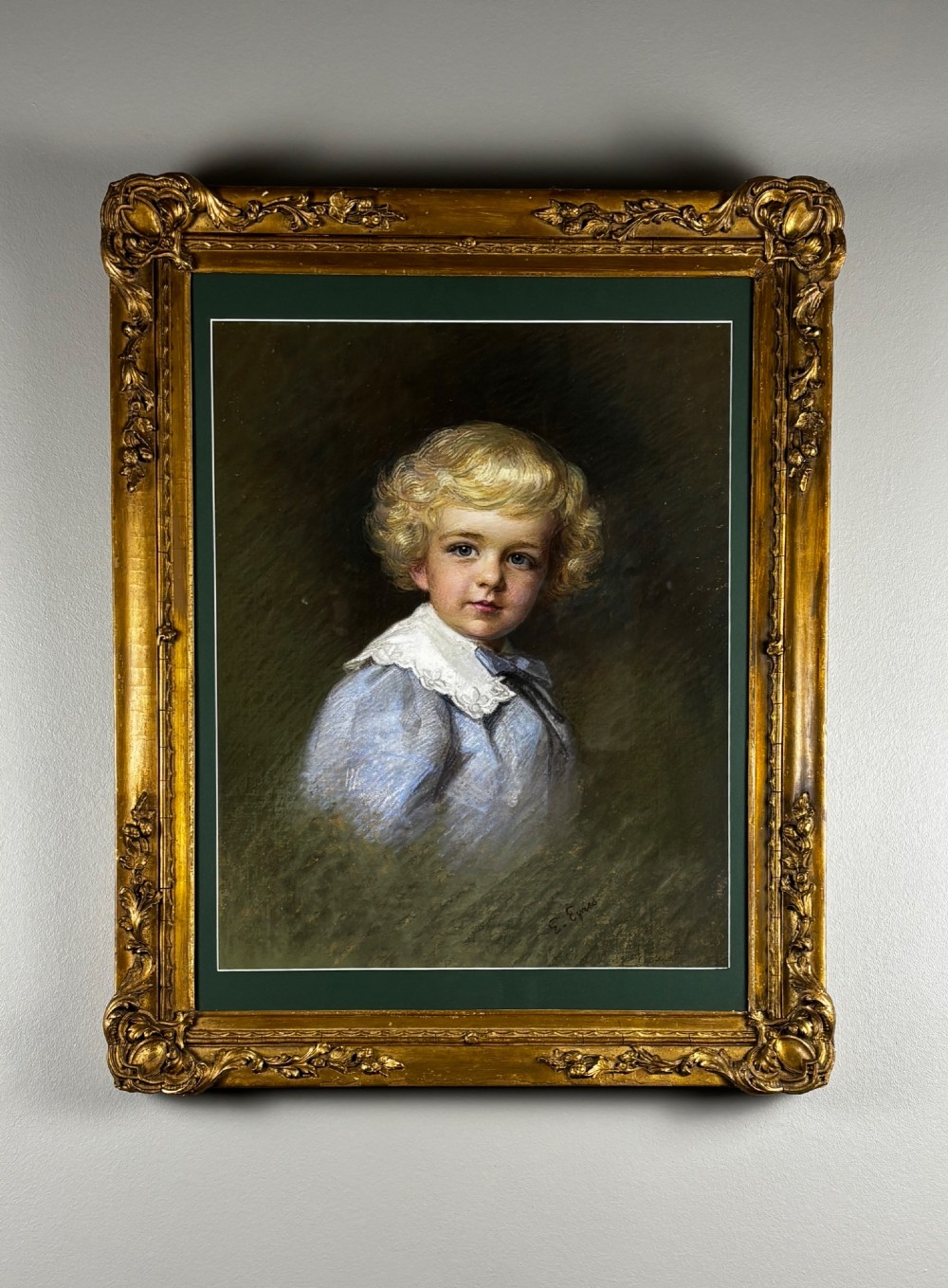 An antique pastel portrait of a blonde young boy wearing a blue garment and lace collar, presented in a dark green mount and an ornate gold gilt frame.