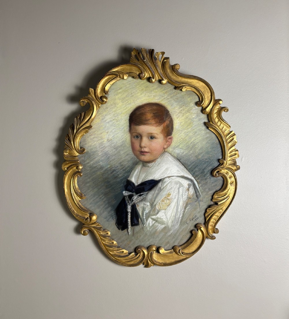 An oval Edwardian portrait of a young boy in a white sailor collar with a navy blue bow, set within a carved giltwood scroll frame.