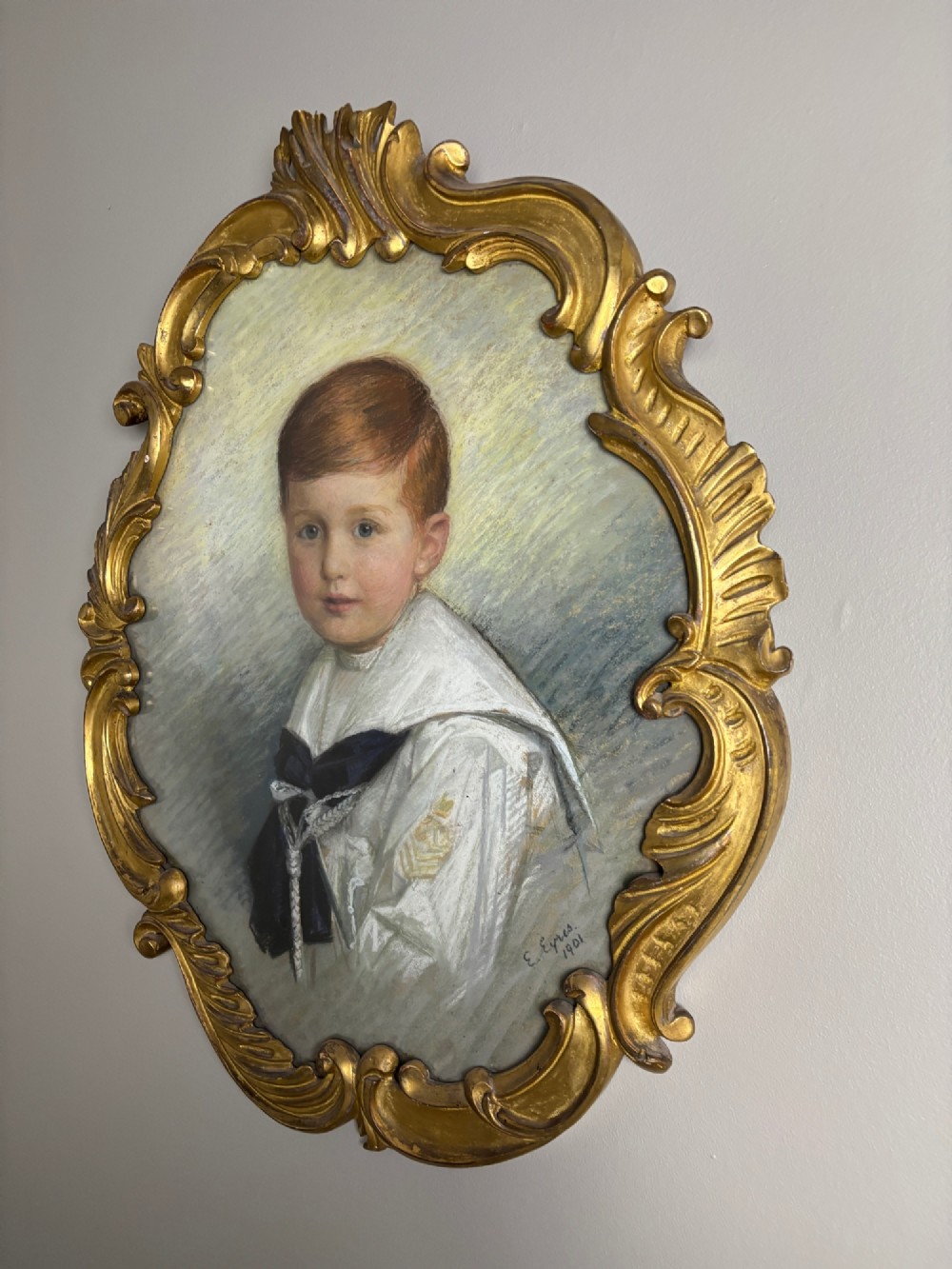 An oval Edwardian portrait of a young boy in a white sailor collar with a navy blue bow, set within a carved giltwood scroll frame. View VI