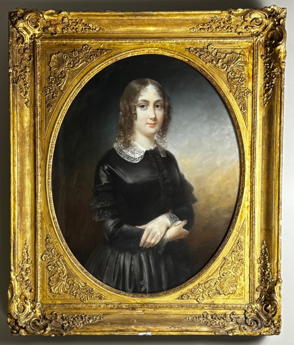 An oil portrait of a dark-haired woman in a black dress housed within an oval spandrel and a heavily carved gilt frame. View II