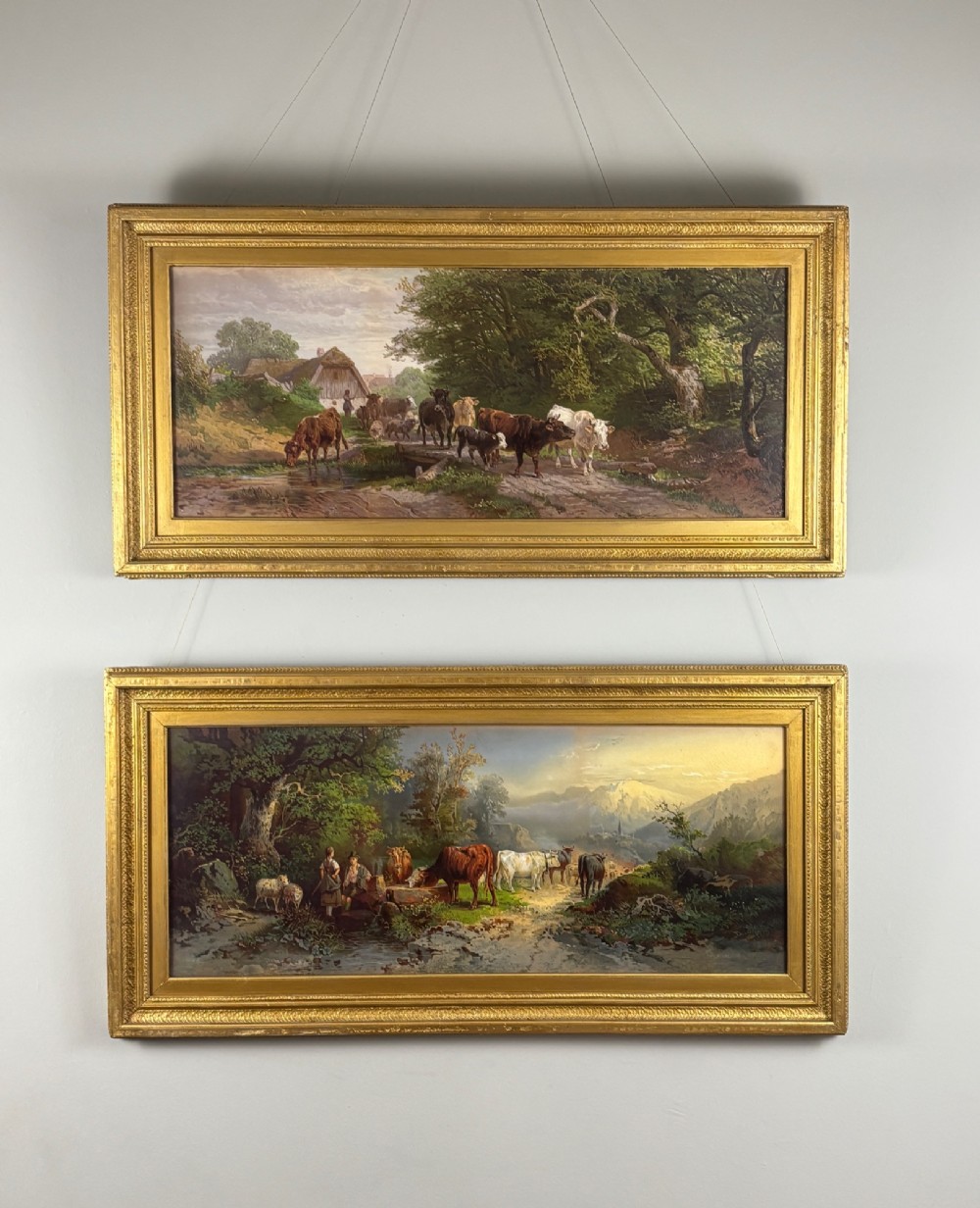 A pair of framed 19th-century pastoral oil paintings depicting rural landscapes with cattle and figures, set within matching giltwood frames.