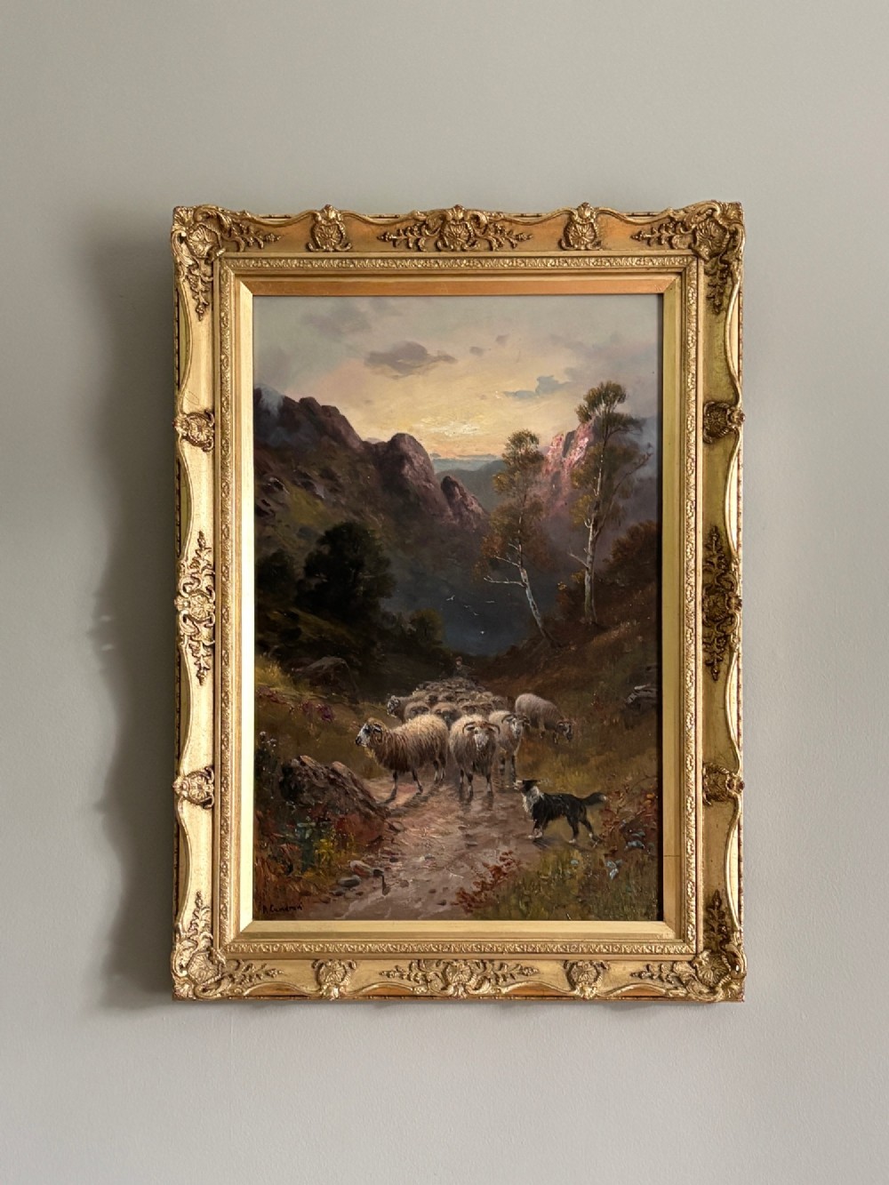 An oil painting on canvas depicting a flock of sheep and a sheepdog on a Scottish mountain path at sunset, presented in an ornate giltwood frame.