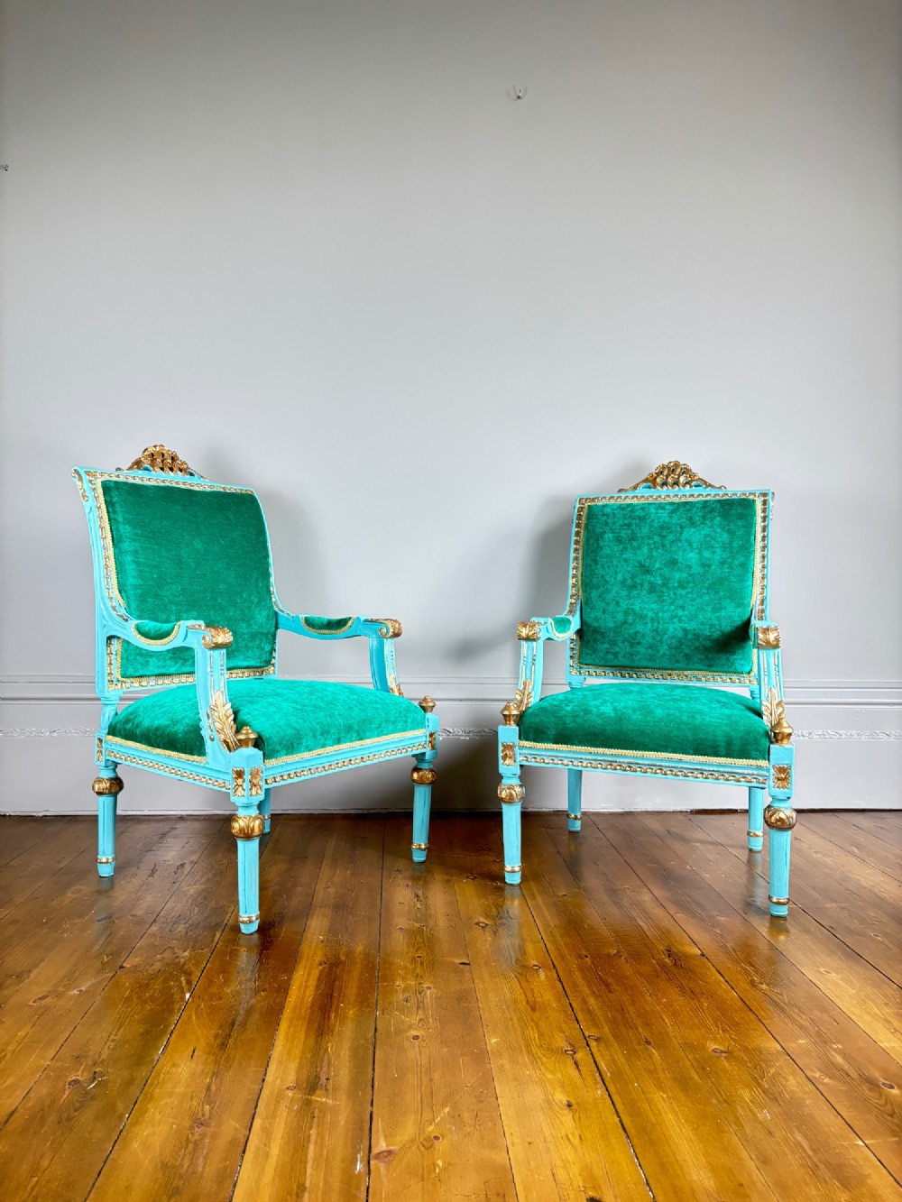 A pair of mid-19th-century French open armchairs featuring turquoise painted frames with gold gilt detailing and emerald green velvet upholstery.