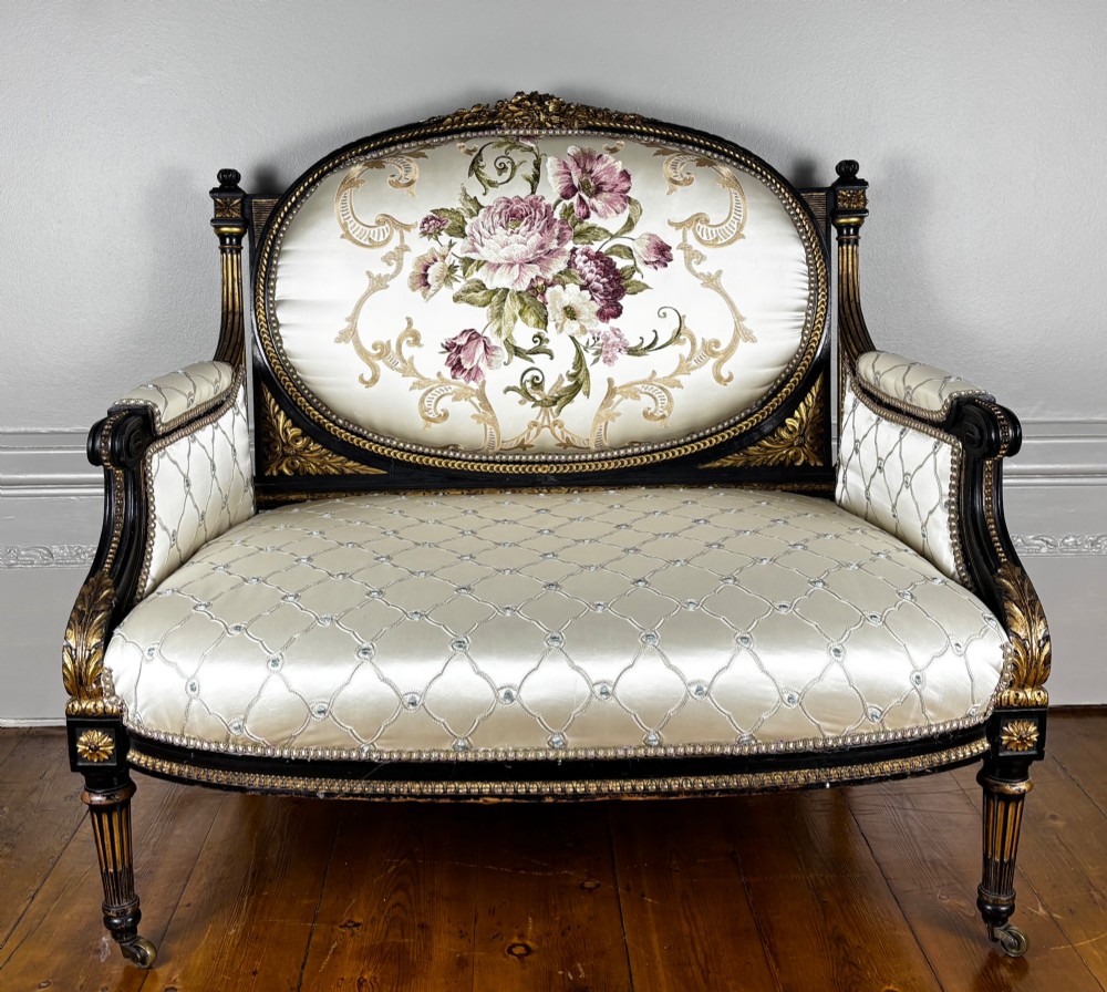 A French Louis XVI style settee featuring an ebonised frame with gilt details and cream silk upholstery.
