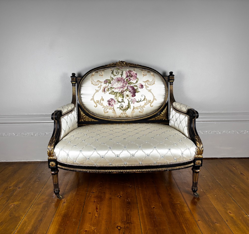 A French Louis XVI style settee featuring an ebonised frame with gilt details and cream silk upholstery. View II
