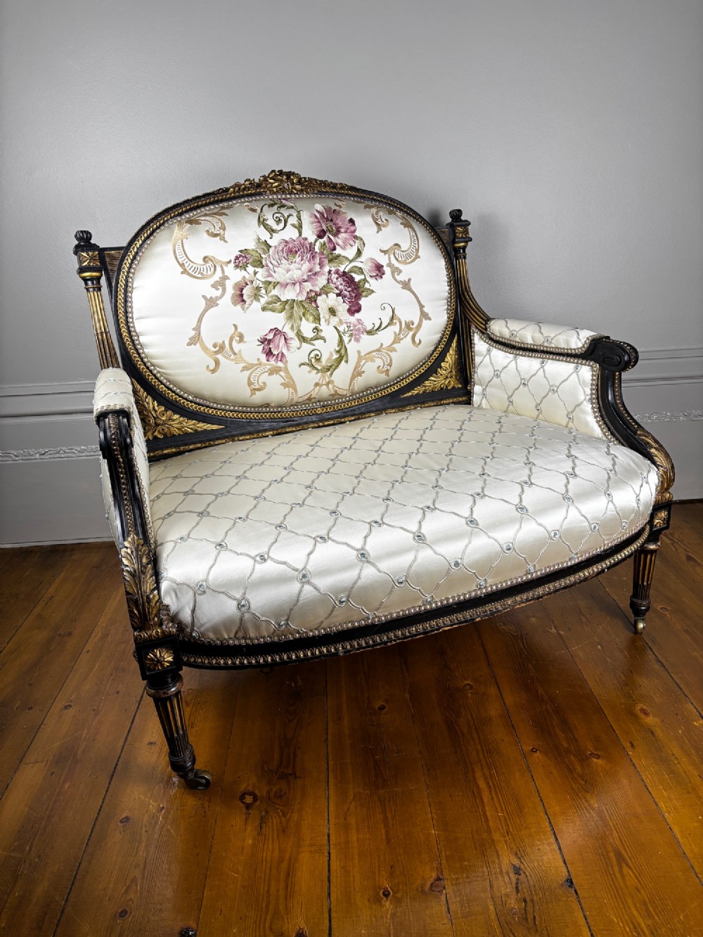 A French Louis XVI style settee featuring an ebonised frame with gilt details and cream silk upholstery. View VI