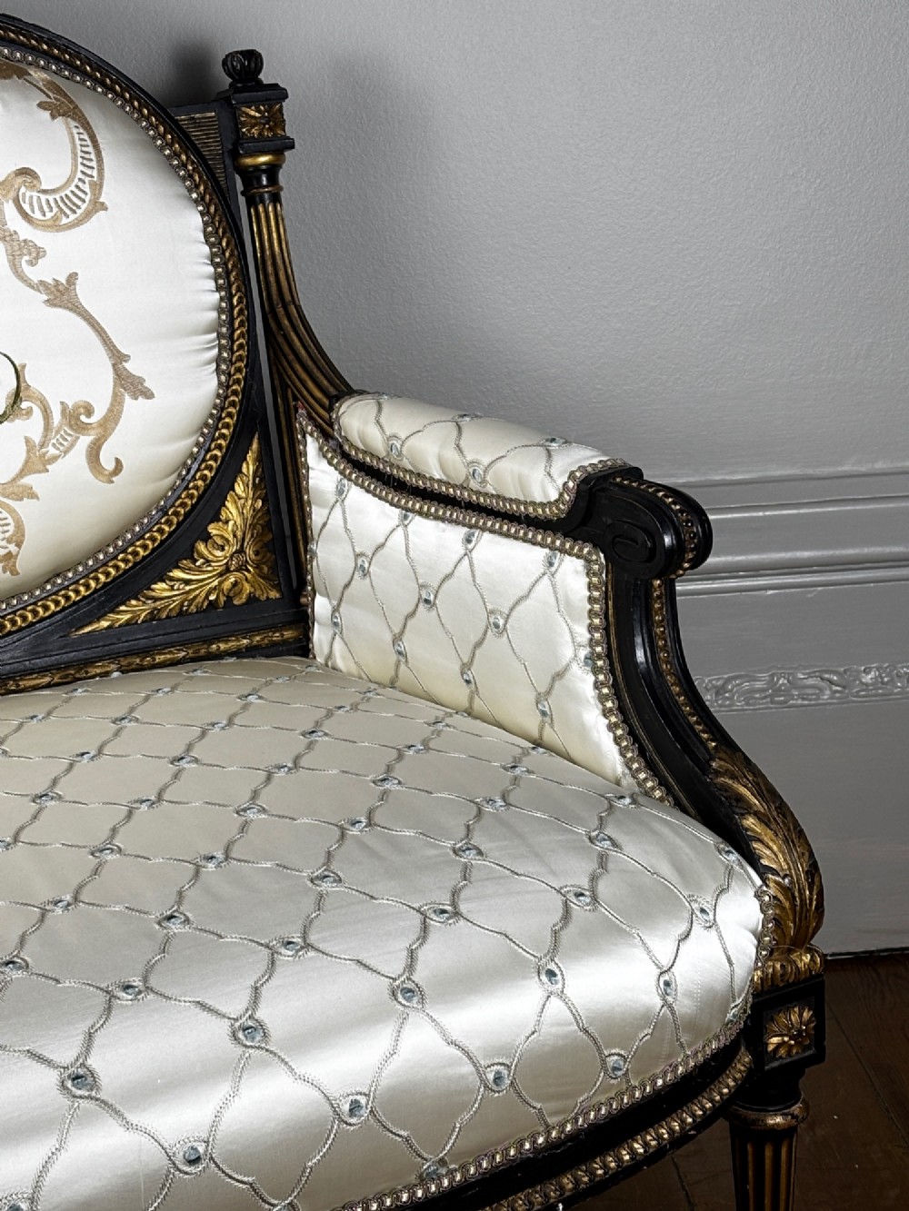 A French Louis XVI style settee featuring an ebonised frame with gilt details and cream silk upholstery. View VII