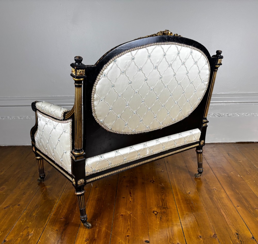 A French Louis XVI style settee featuring an ebonised frame with gilt details and cream silk upholstery. View IX