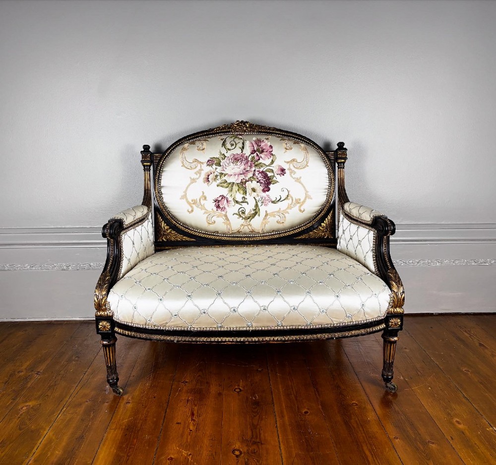 A French Louis XVI style settee featuring an ebonised frame with gilt details and cream silk upholstery. View X